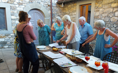 Artist Marianne Ryan with her students standing around the table reviewing the days painting whilst enjoying a pre-dinner aperitivi